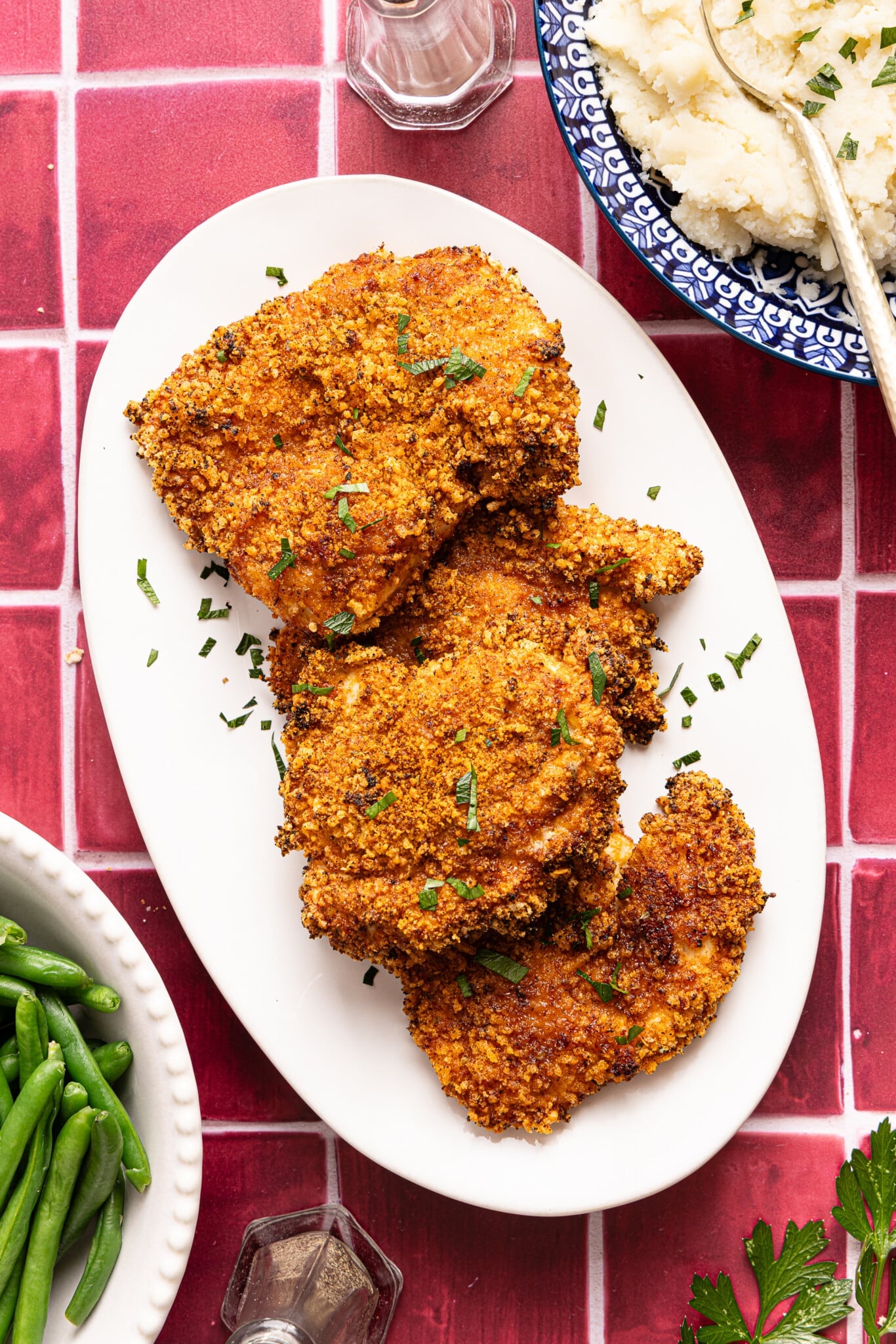 Air fryer chicken cutlets on a white serving platter on a red tile countertop.
