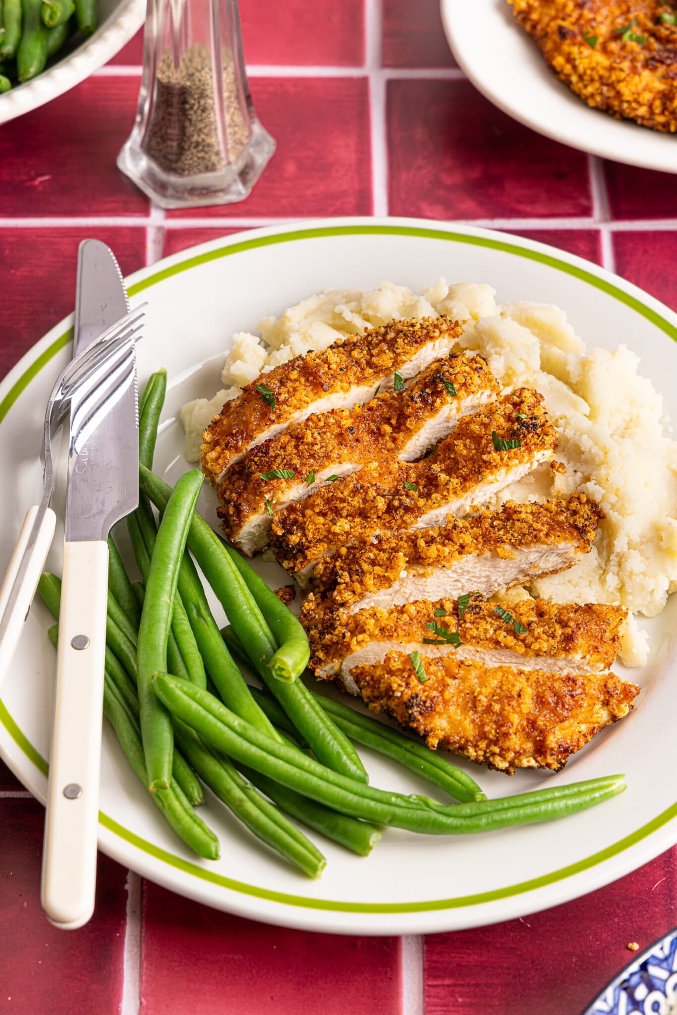 A sliced air fryer chicken cutlet on a plate with mashed potatoes and green beans.