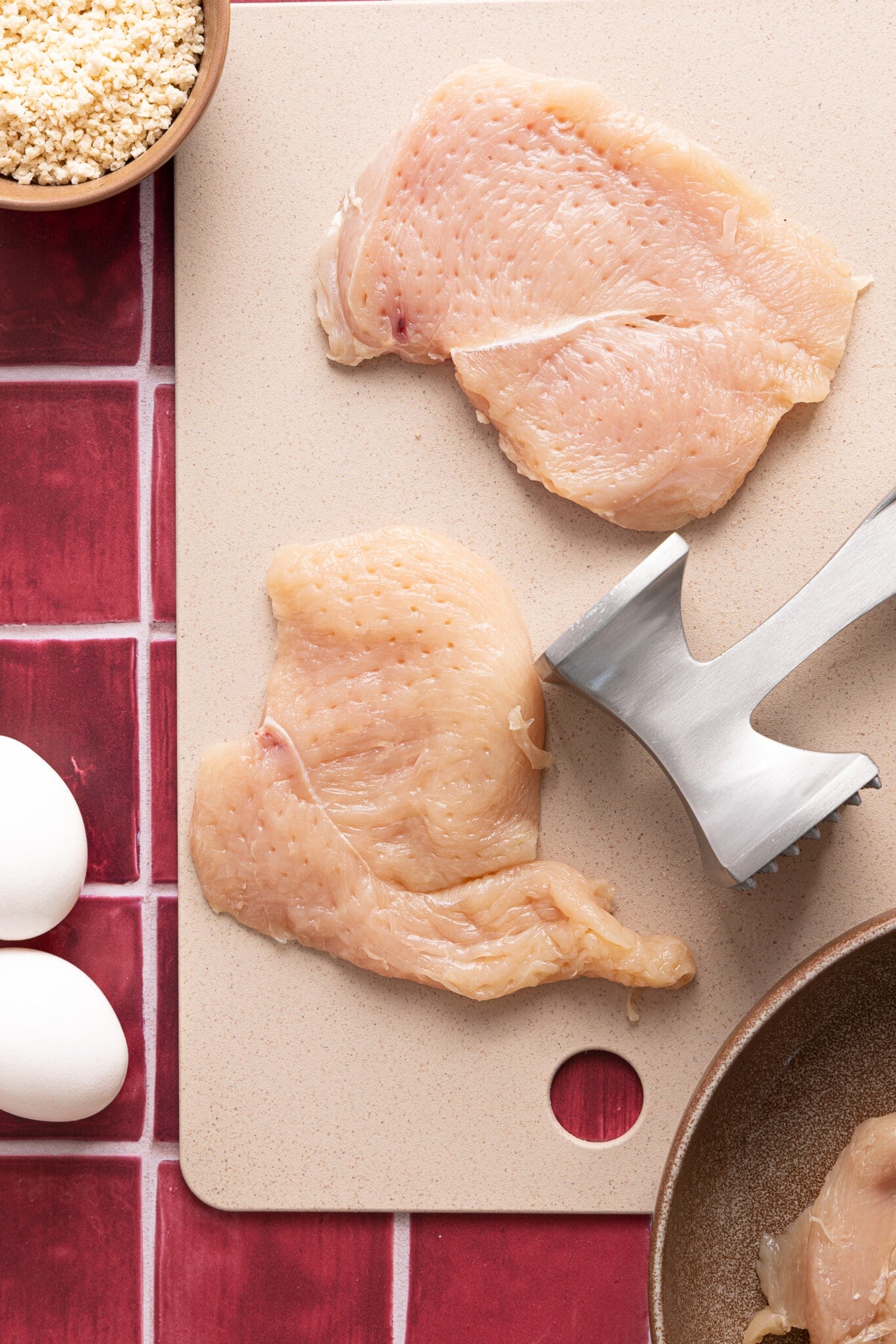 Two pounded chicken cutlets on a cutting board.
