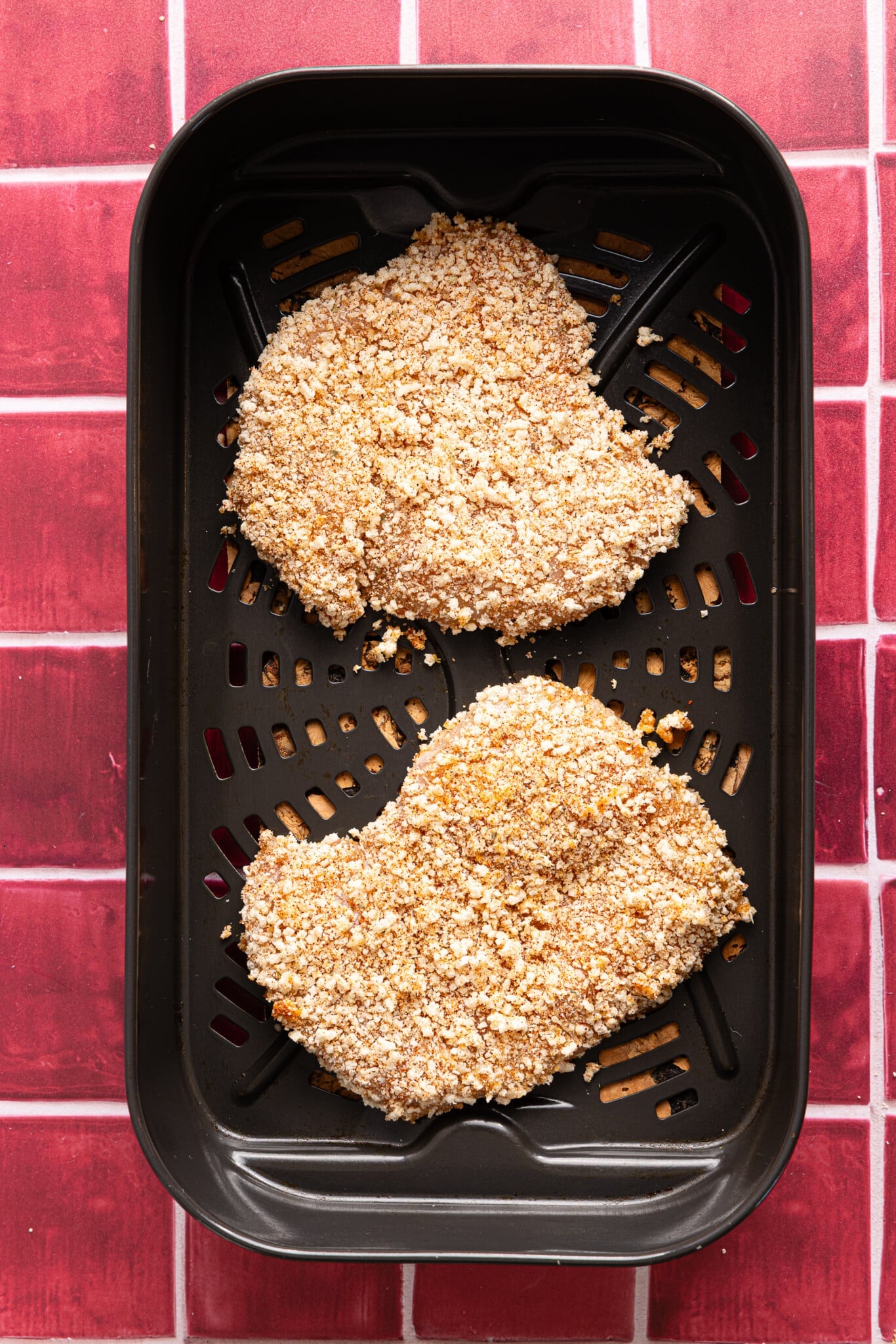 The coated chicken cutlets in the air fryer basket before cooking.