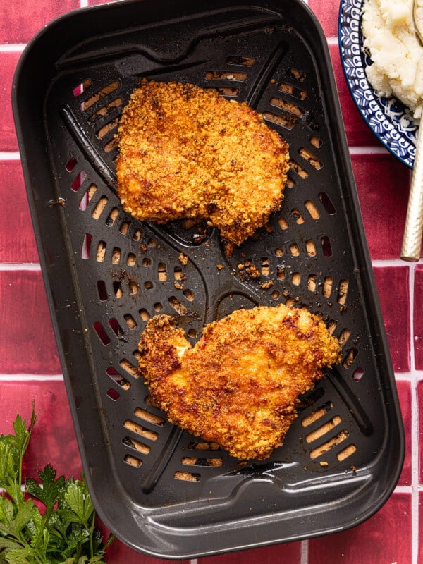 The cooked chicken cutlets in the air fryer basket on a countertop.