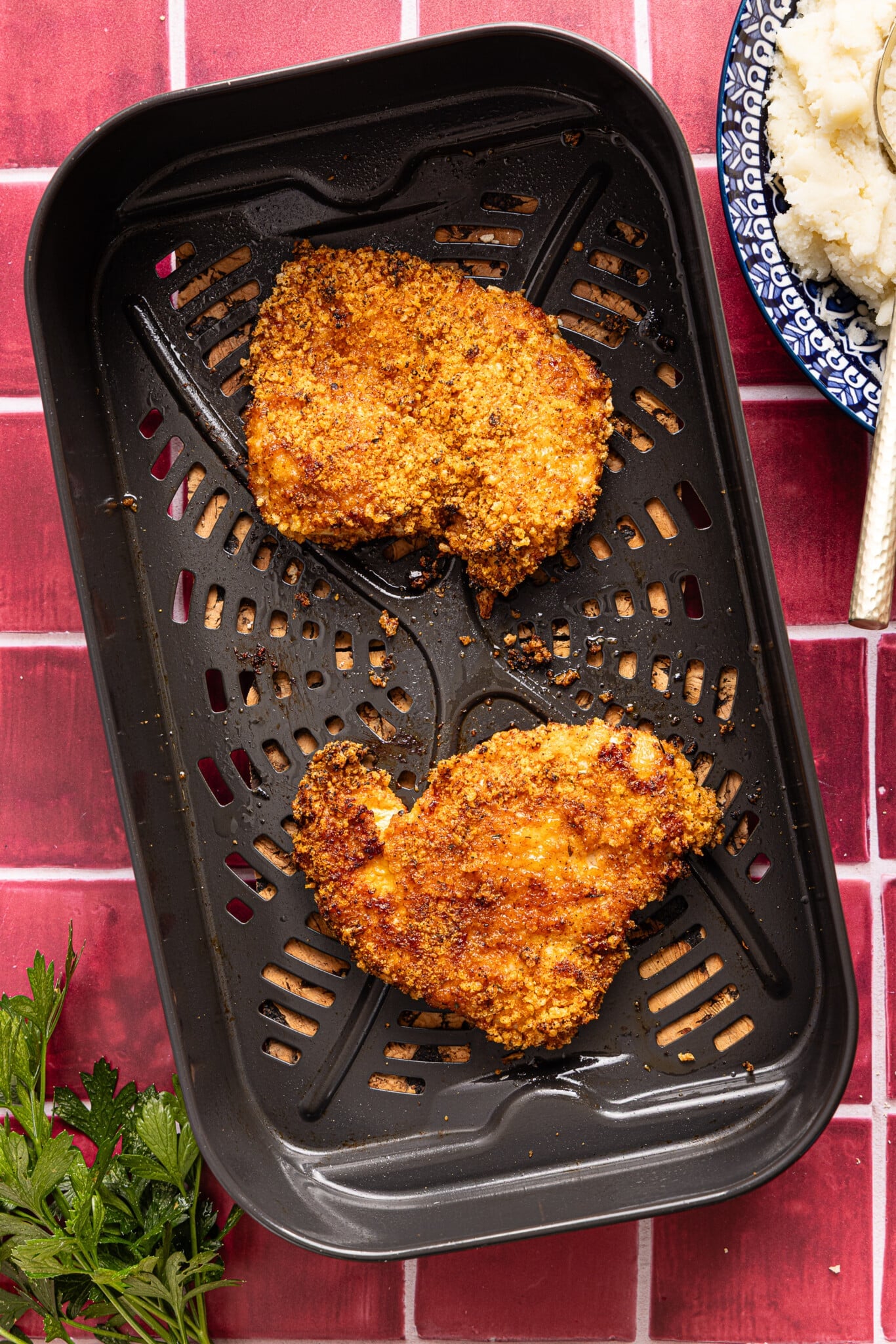 The cooked chicken cutlets in the air fryer basket on a countertop.