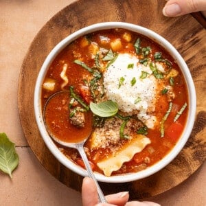 A bowl filled with slow cooker lasagna soup and topped with a dollop of the cheese topping and fresh chopped basil.
