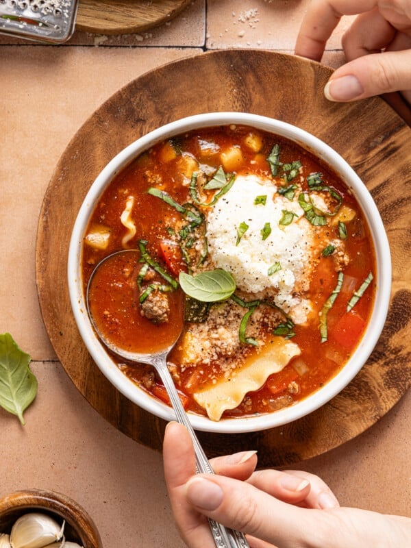 A bowl filled with slow cooker lasagna soup and topped with a dollop of the cheese topping and fresh chopped basil.