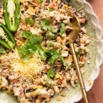 Southwest chicken salad in a bowl with a spoon. A sliced jalapeno, chopped cilantro and shredded Mexican cheese blend are garnished on top.