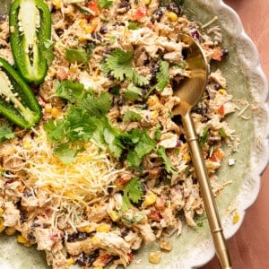 Southwest chicken salad in a bowl with a spoon. A sliced jalapeno, chopped cilantro and shredded Mexican cheese blend are garnished on top.