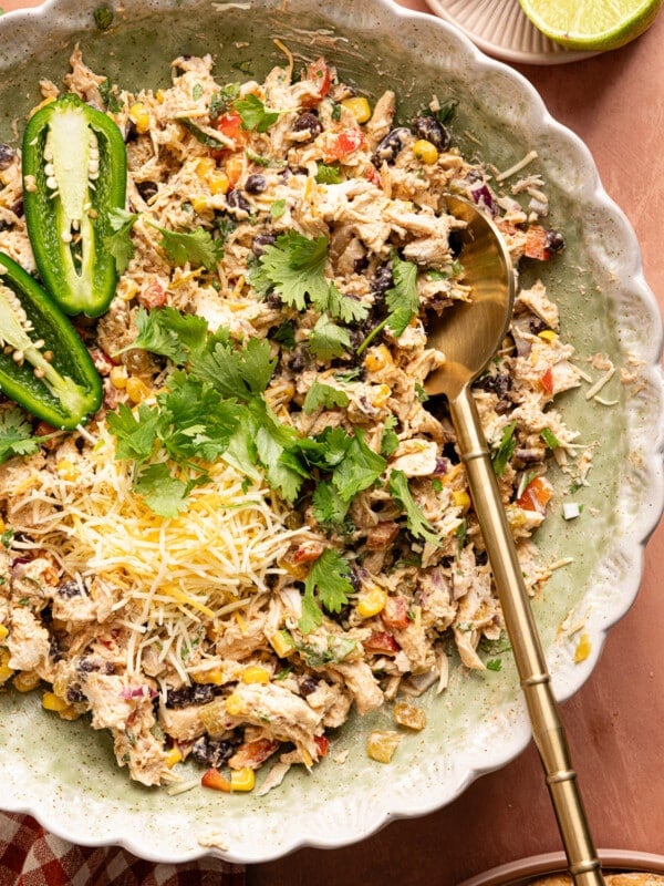 Southwest chicken salad in a bowl with a spoon. A sliced jalapeno, chopped cilantro and shredded Mexican cheese blend are garnished on top.